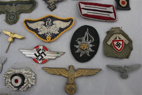 A collection of various German Third Reich cap badges, cloth badges and pins